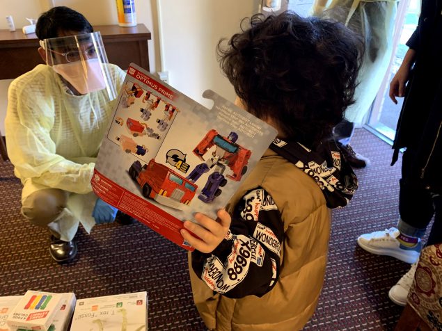 A medical officer wearing PPE giving a toy to a child in quarantine